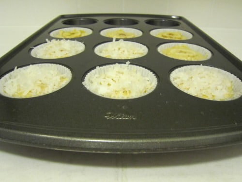 Muffin tin filled with banana orange coconut muffin batter, topped with shredded coconut and ready for baking.