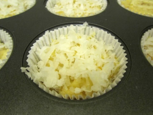 Shredded coconut topping unbaked banana orange muffin batter in a lined muffin tin.