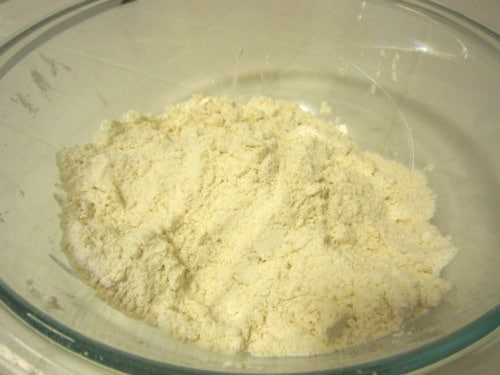 Dry ingredients including flour, sugar, baking powder, and baking soda mixed in a clear glass bowl for Irish soda bread muffins.