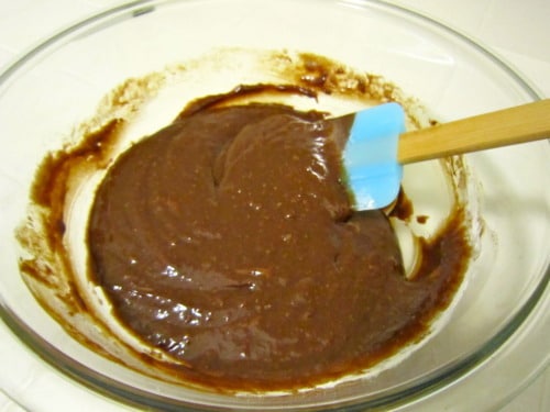 Chocolate batter being mixed in a glass bowl with a blue silicone spatula.