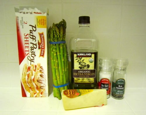 Ingredients arranged for making an asparagus and gruyere tart, including puff pastry, fresh asparagus, olive oil, seasonings, and cheese.