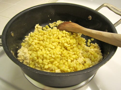 Diced tofu and corn cooking in a black skillet with a wooden spoon on the stovetop.