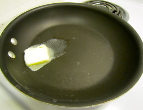 Pat of butter melting in a nonstick skillet on a stovetop, preparing the pan for cooking pancakes.