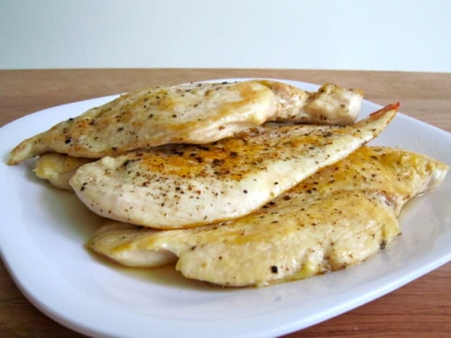 Seasoned chicken breasts cooked until golden and plated on a white dish, ready to be added to chicken noodle soup.