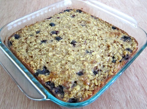 Freshly baked blueberry oatmeal in a square glass baking dish, with a golden oat topping and blueberries visible throughout.