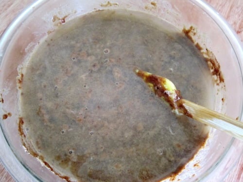 Chocolate cupcake batter being mixed in a glass bowl with a wooden spoon.