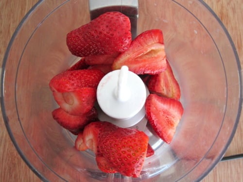 Halved fresh strawberries in a food processor, ready to be blended for chocolate cupcakes with fresh strawberry frosting.