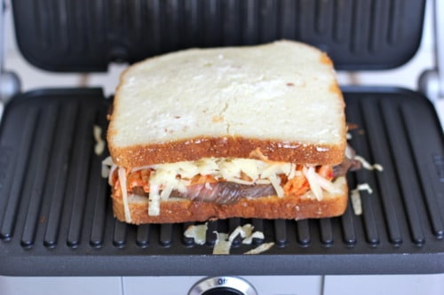 Sandwich with shredded vegetables and cheese being grilled in a panini press.