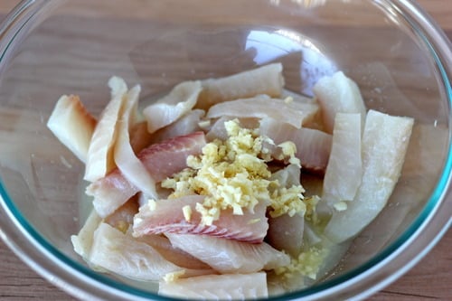 Sliced raw fish with minced garlic and ginger in a glass bowl, prepared for biscuit lime fish tacos.