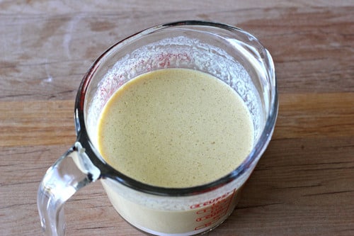 Mocha oatmeal muffin batter in a glass measuring cup on a wooden surface.