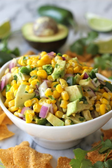 Bowl of avocado corn salsa with red onion, jalapeño, and cilantro, served with tortilla chips.