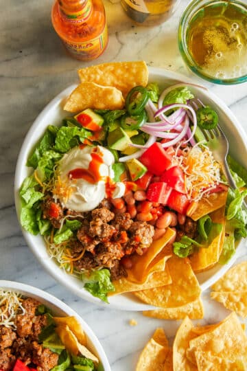 Taco salad served in a crispy tortilla bowl, filled with lettuce, ground beef, black beans, tomatoes, cheese, olives, and topped with sour cream.