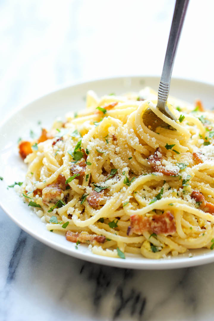 Close-up of a creamy bowl of spaghetti carbonara, topped with crispy pancetta and freshly ground black pepper, served with a fork resting on the side.