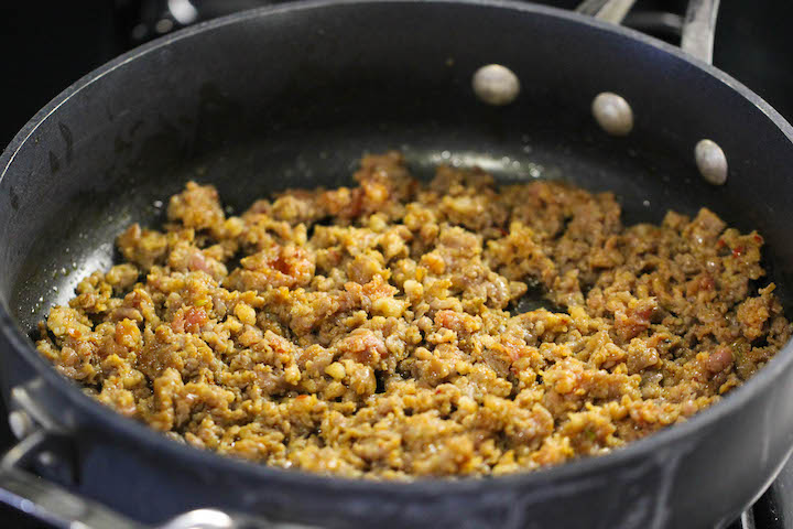 Cooked ground sausage browning in a black nonstick skillet on a stovetop.
