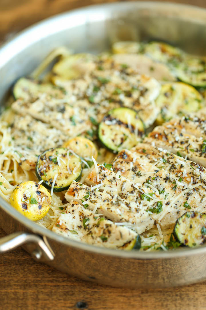 Garlic butter fettuccine topped with grilled chicken, zucchini, and yellow squash, garnished with herbs and shredded Parmesan in a stainless steel skillet.