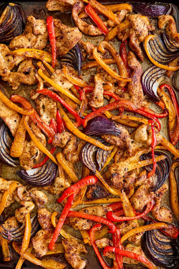 Chicken fajitas on a flour tortilla with roasted bell peppers, red onions, sliced chicken, fresh cilantro, and a lime wedge.