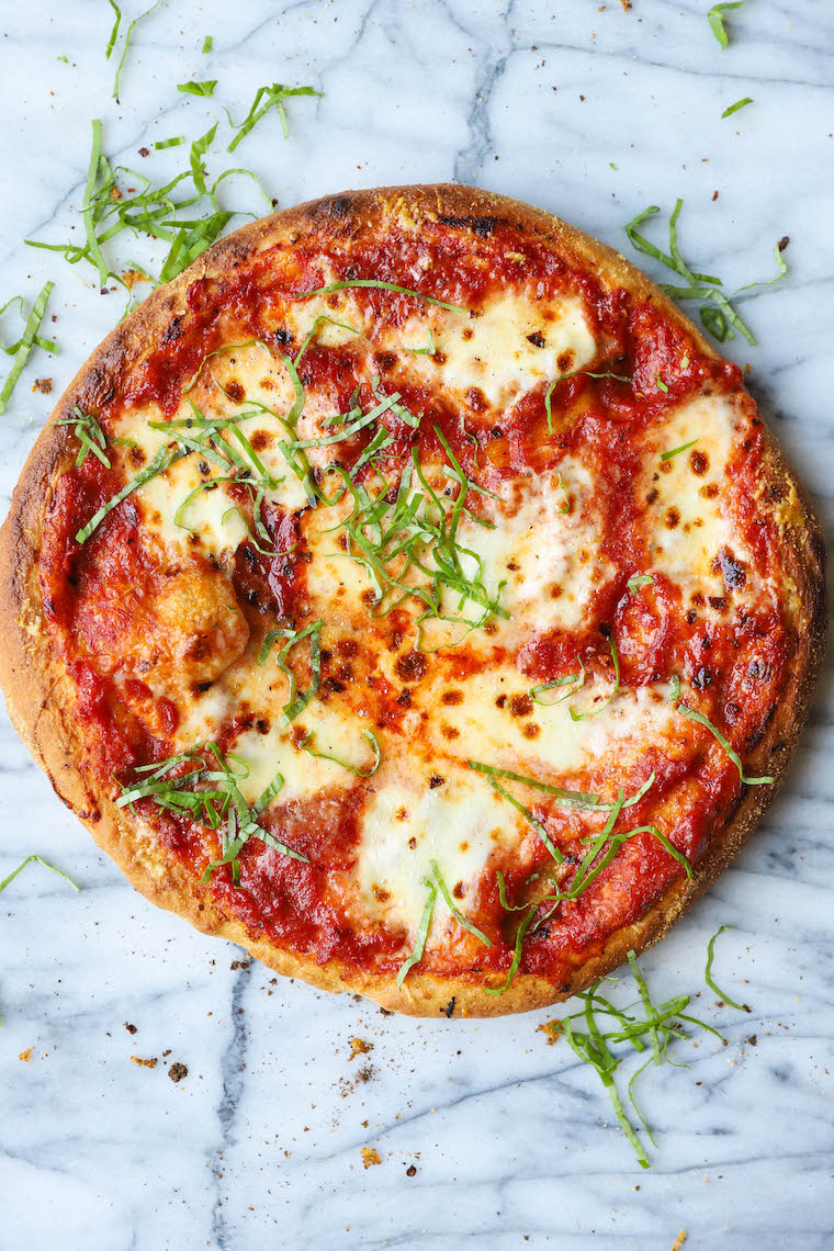 Ball of homemade pizza dough on a floured surface, ready to be rolled out, with a wooden rolling pin and a dusting of flour visible in the background."