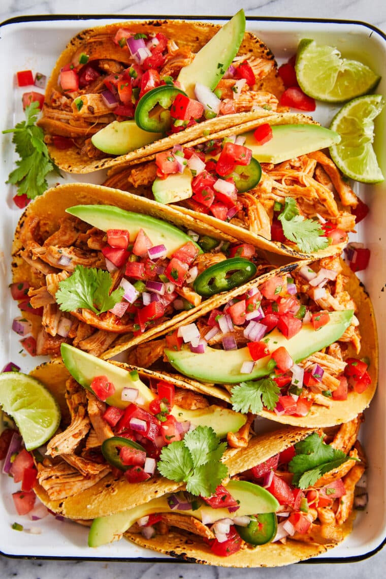 chicken tacos instant pot with avocado, pico de gallo, cilantro, and lime wedges.