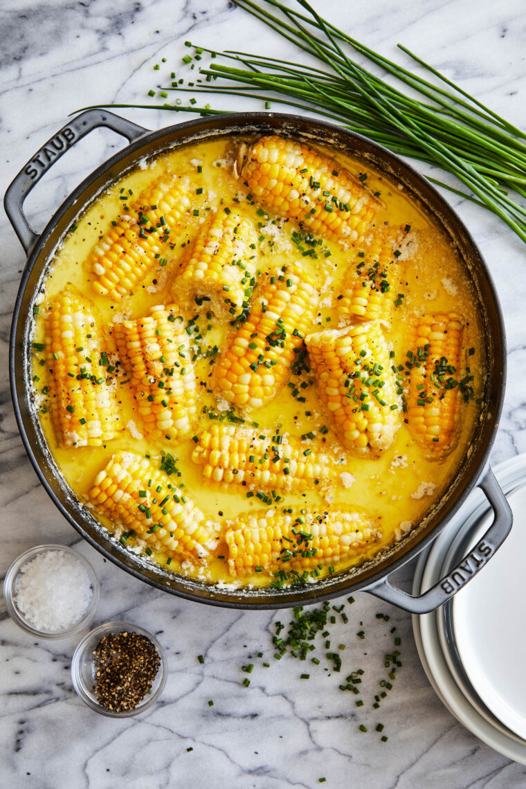 Boiled corn on the cob topped with melting butter and chopped herbs, arranged on a platter.